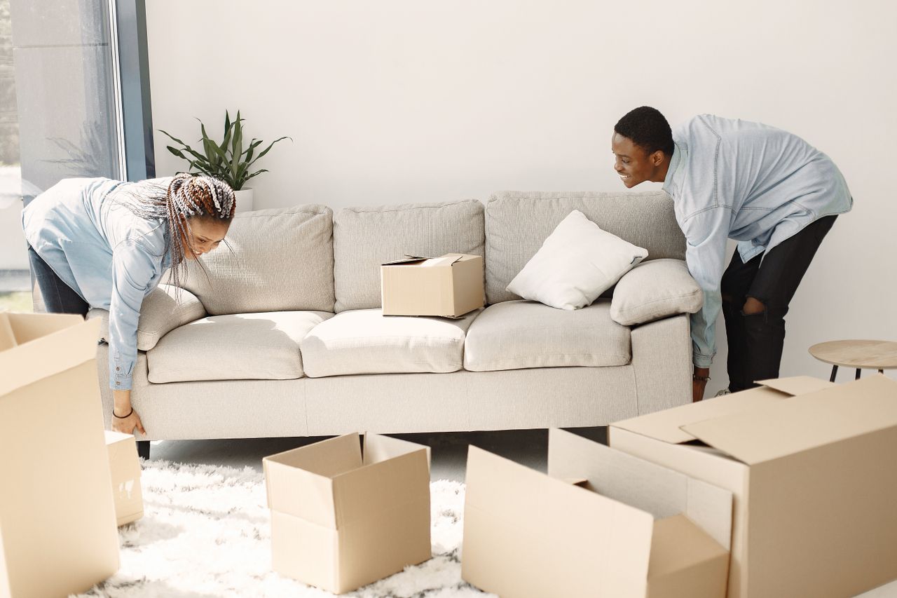 services-03 Happy couple arranging a sofa in their new home, with moving boxes all around them.
